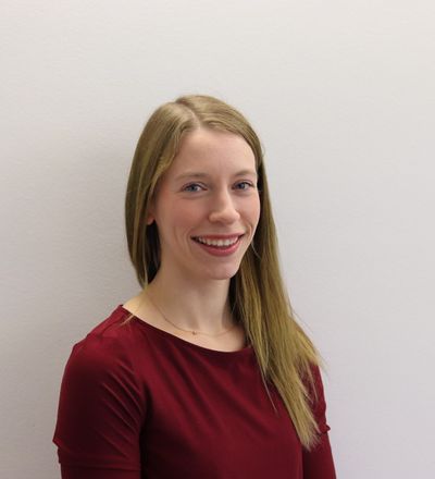 Julia Lücking lächelnd in dunkelrotem Oberteil vor heller Wand
